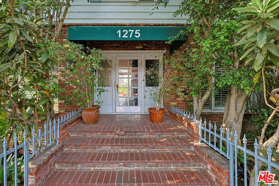 Front view of a building with a brick exterior and steps leading to an entrance with a glass door.
