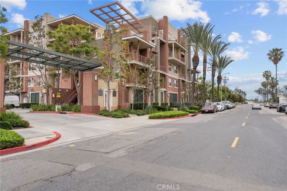 Front view of a multi-story apartment building with balconies and palm trees along the street.