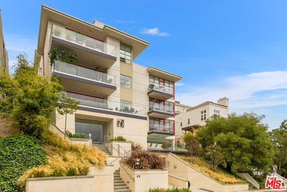 Front view of a multi-story modern building with balconies and a sloped entrance.