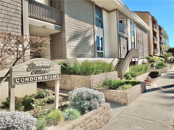 Front view of a condominium complex with a wooden sign and landscaped walkway.