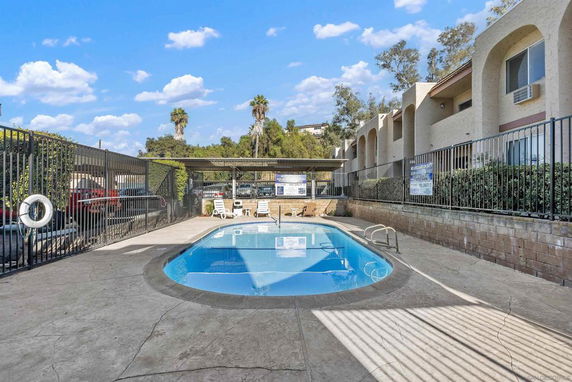 Outdoor swimming pool area surrounded by fencing and adjacent buildings.