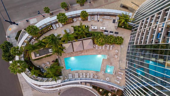 Aerial view of a modern rooftop area with a swimming pool and seating arrangements next to a glass-walled building.