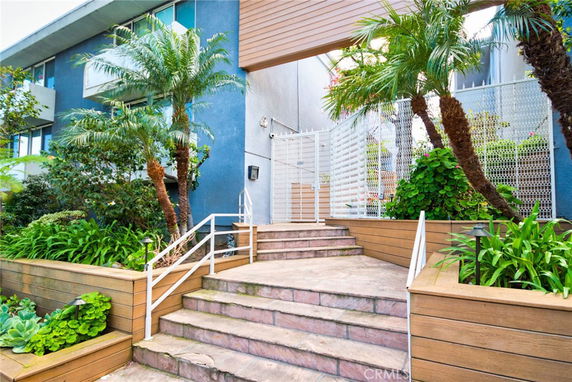 Entrance view of a multi-story building with stairs and greenery.