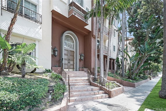 Front view of a multi-story building entrance with stairs and surrounding greenery.