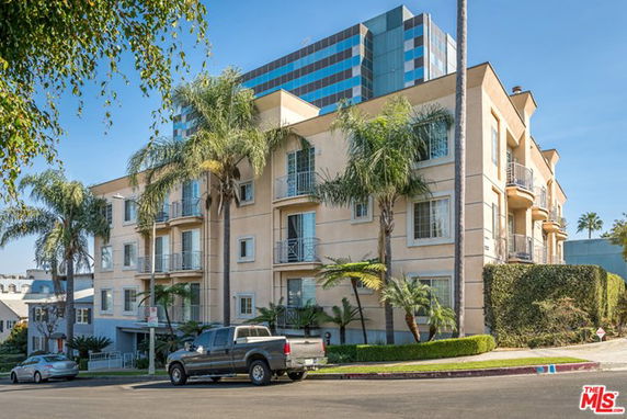 Front view of a multi-story apartment building with balconies and palm trees.