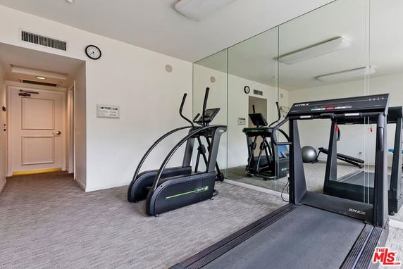 Indoor gym area with exercise equipment and mirrors on the wall.