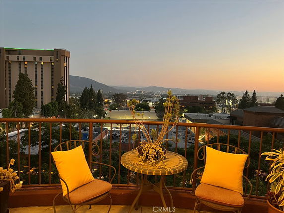 Panoramic view from a balcony with a table and chairs, overlooking a cityscape at dusk.