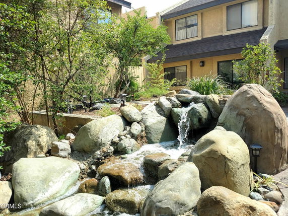 Front view of a two-story house with stone accents and a waterfall feature in the garden.