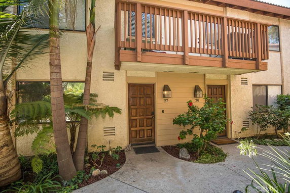 Front view of a two-story building with wooden balcony and dual entrance doors.