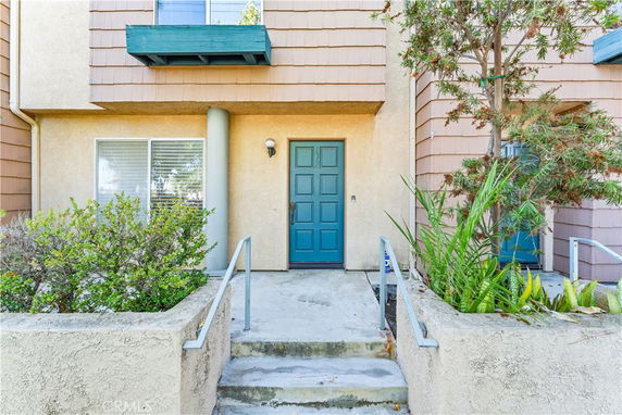 Front view of a building entrance with a blue door and surrounding foliage.
