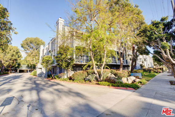 Front view of a multi-story residential building with balconies and surrounded by trees.