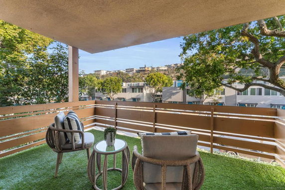 Balcony with chairs and table overlooking residential buildings and trees.
