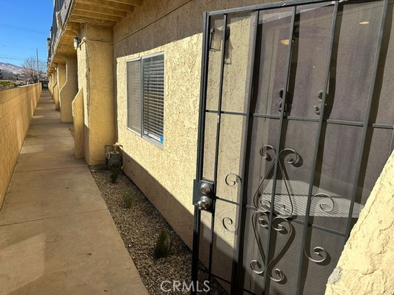 Front view of a building with yellow stucco walls, a metal security door, and a sidewalk leading to the entrance.