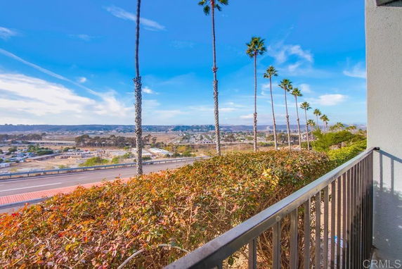 Balcony view overlooking a road and open landscape with palm trees.