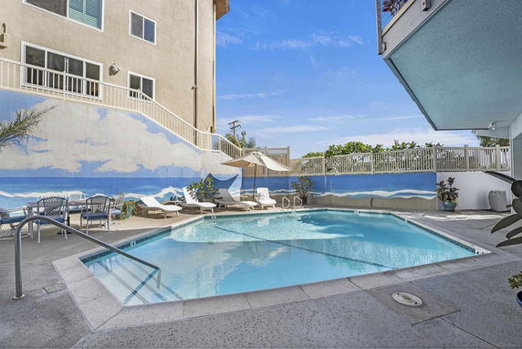 Outdoor view of a swimming pool area with lounge chairs, umbrellas, and a mural wall.