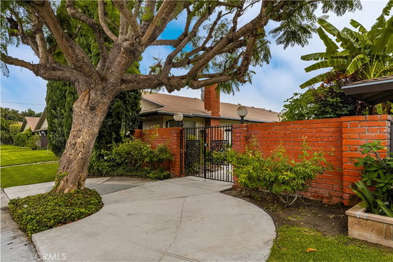 Front view of a house with a brick wall and gate, surrounded by greenery and trees.