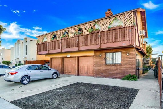 Front view of a two-story house with wooden balcony and garage doors.