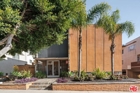 Front view of a building with a modern facade and tall palm trees.