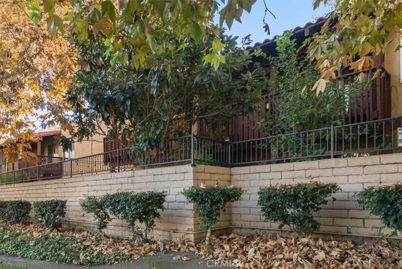 Front view of a house with a brick and iron fence and foliage.