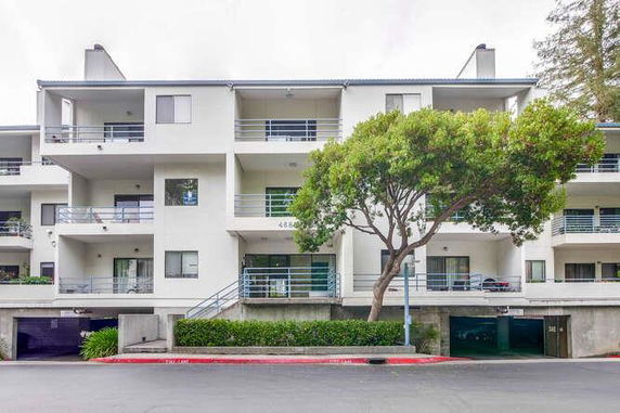 Front view of a multi-story apartment building with balconies and a tree in front.