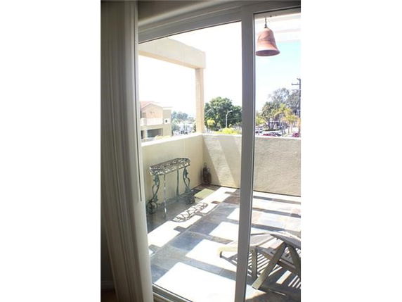 View from a balcony through a glass door showing surrounding areas with trees and buildings.