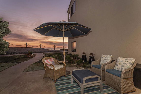 Outdoor seating area with wicker chairs and umbrella overlooking a path and the horizon.