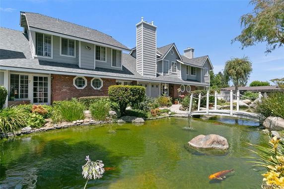 Front view of a two-story house with a brick and gray exterior, featuring multiple windows and a pond with a small bridge.
