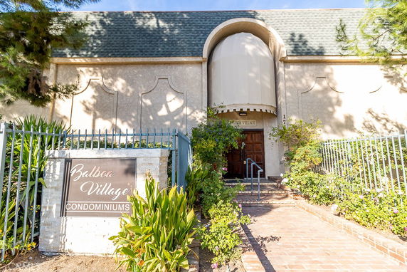 Front view of a condominium building with a sign reading 'Balboa Village Condominiums' and an entrance surrounded by greenery.