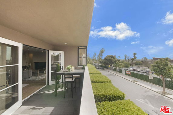 View from a balcony overlooking a street and trees with outdoor seating.