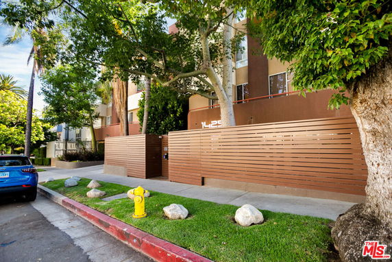 Front view of a multi-story building with a modern fence and trees.