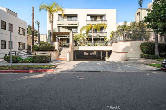 Front view of a multi-story residential building with an entrance staircase and landscaping.