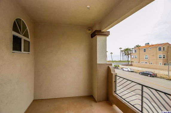 Balcony view overlooking a street with ocean and palm trees in the background.