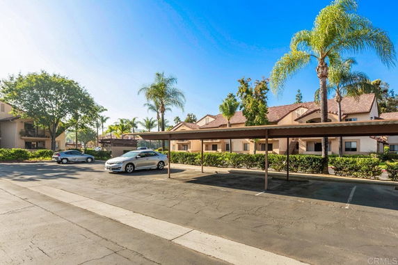 Outdoor parking area with covered parking spaces near residential buildings.