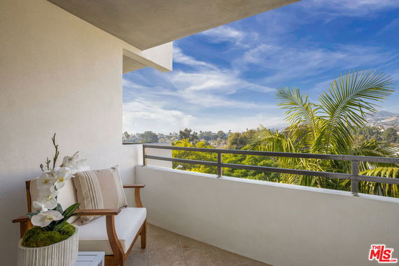 Balcony view overlooking trees and distant hills under a clear blue sky.
