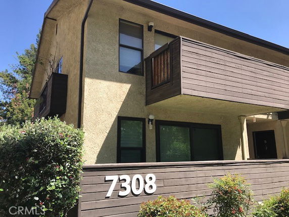 Front view of a two-story building with a wooden balcony and house number 7308.