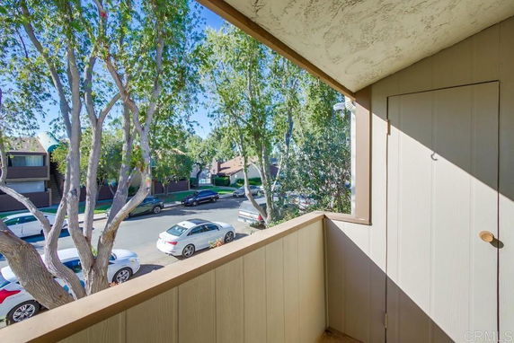 View from a balcony overlooking a street with parked cars and trees.