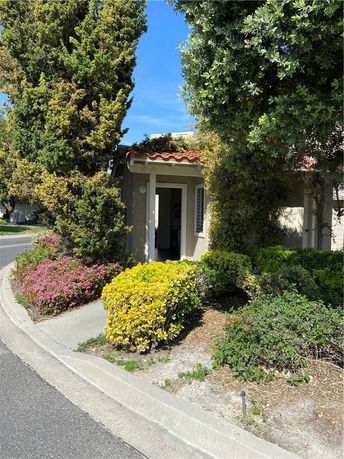 Front view of a house with a tiled roof partially obscured by trees and shrubs.