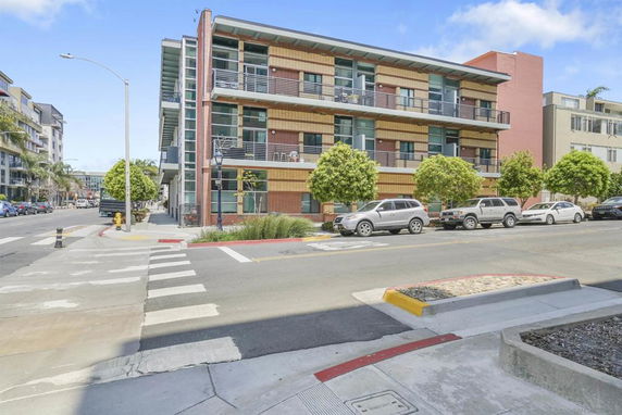 Front view of a modern multi-story building with balconies and parked cars.