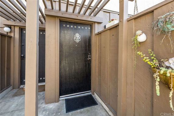 Front view of a building entrance with a wooden door and pergola structure.