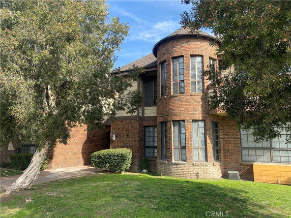 Front view of a brick house with large rounded windows and trees in the foreground.