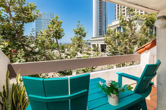 View from a balcony with a table and chairs, overlooking trees and city buildings.