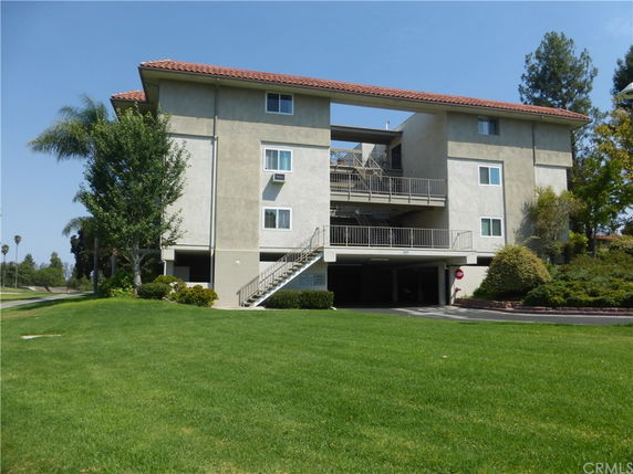 Front view of a multi-story apartment building with an outdoor staircase and parking area.