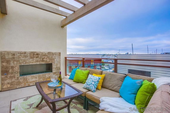 Rooftop patio with a seating area and a partial fireplace, overlooking a cityscape.