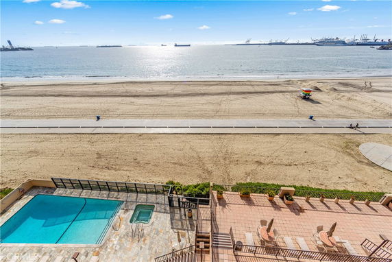 View of a beach and ocean with a swimming pool and patio area in the foreground.