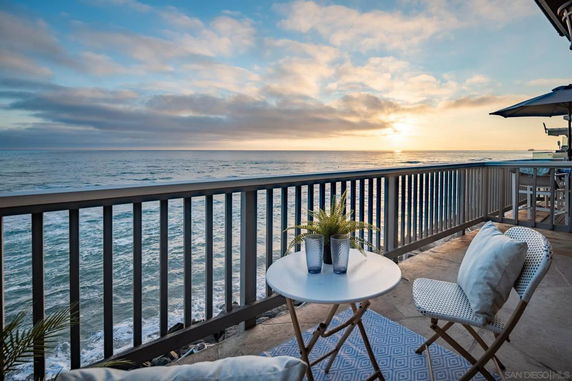 View from a patio overlooking the ocean at sunset with chairs and a table.