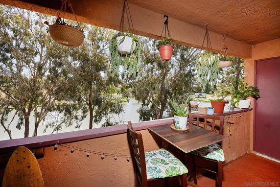 Balcony with plants overlooking trees and a water body.
