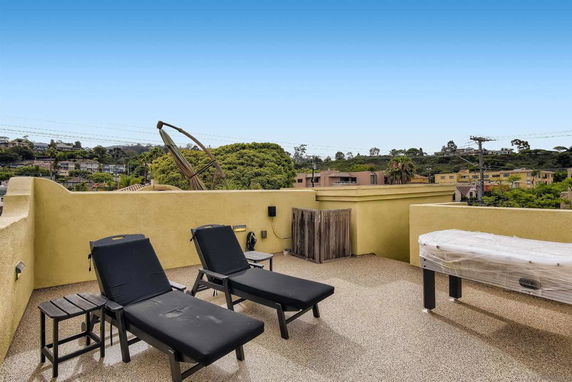 Rooftop area featuring lounge chairs and a table, with a view of surrounding buildings and greenery.