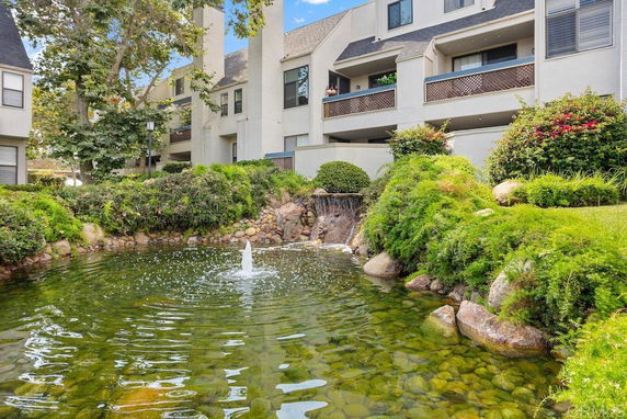 View of a building with balconies and a pond with a fountain in the foreground.