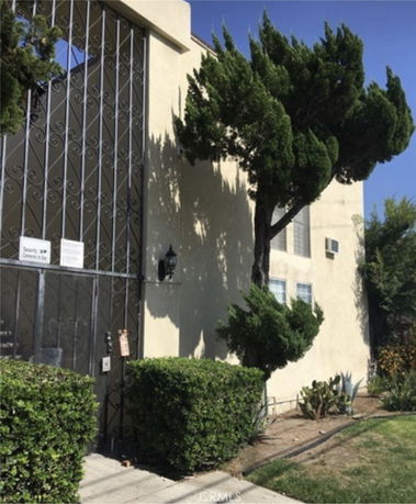 Front view of a multi-story building with trees and a gated entrance.