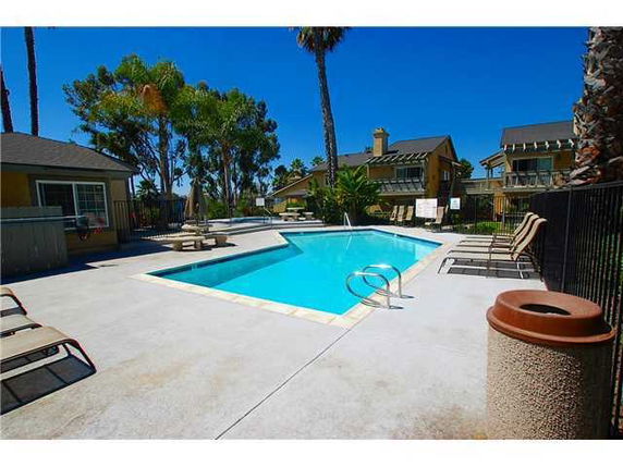 Outdoor swimming pool area with surrounding lounge chairs and nearby buildings.